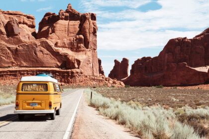 How to Plan a Road Trip A yellow vintage van driving on a scenic road trip highway through red rock canyons in the USA