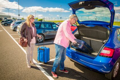 Senior couple loading suitcase into car boot at airport parking lot before a travel trip