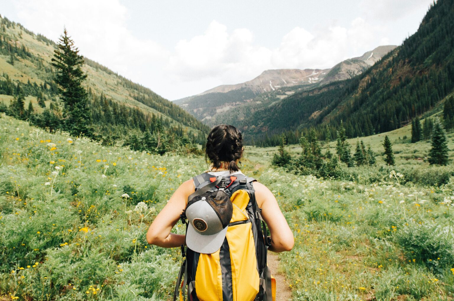 Solo travel tips in action — female traveler with yellow backpack hiking a scenic mountain valley trail