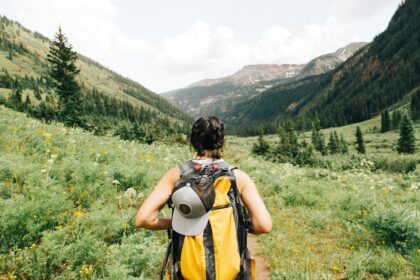 Solo travel tips in action — female traveler with yellow backpack hiking a scenic mountain valley trail