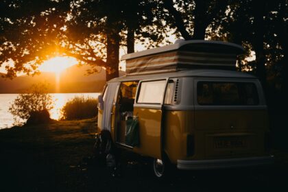 Yellow camping van parked near a lake at sunset with trees and warm golden light