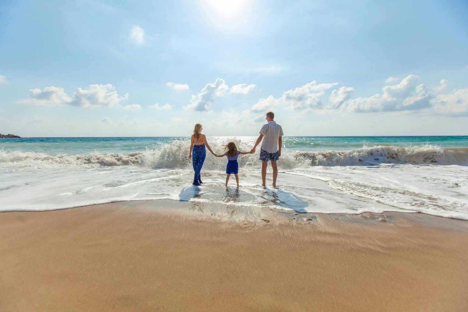 Family standing on a sunny beach with ocean waves and a bright sky