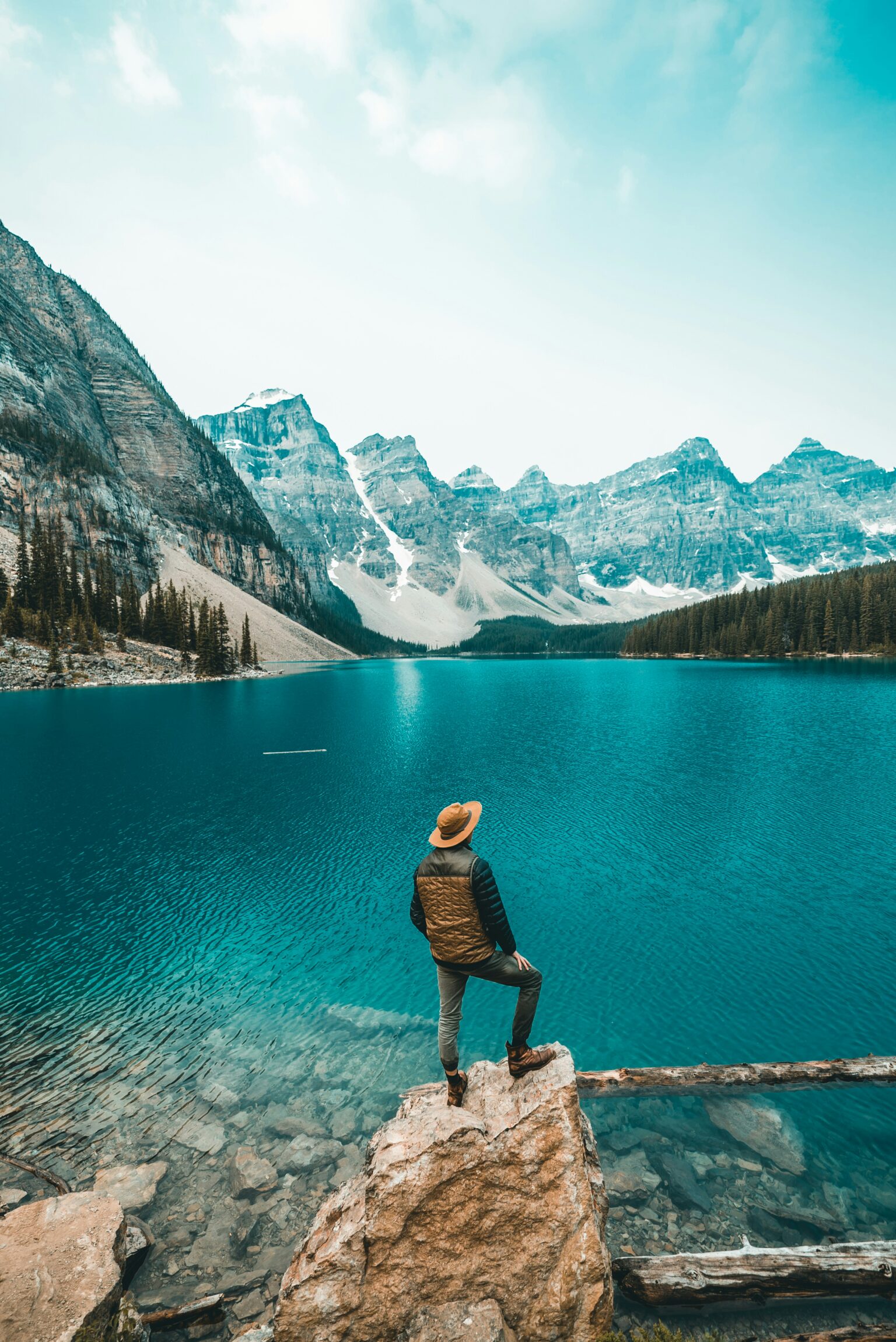 Solo traveler standing on a rock overlooking a turquoise mountain lake.