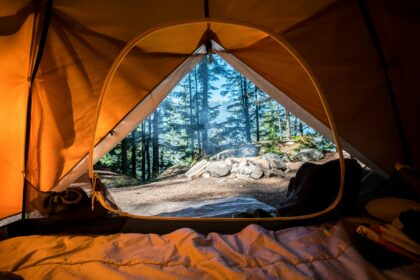 Camping essentials inside a tent with a forest and campsite view outside.