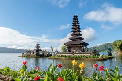 Peaceful lakeside temple in Bali surrounded by flowers under a bright blue sky – Bali travel guide.