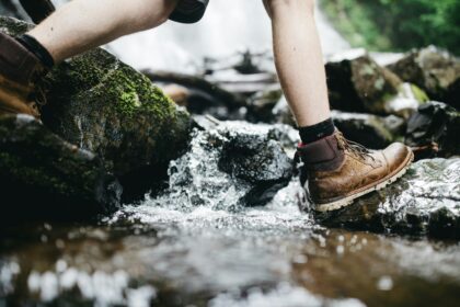 Hiker wearing muddy boots crossing rocks in a stream