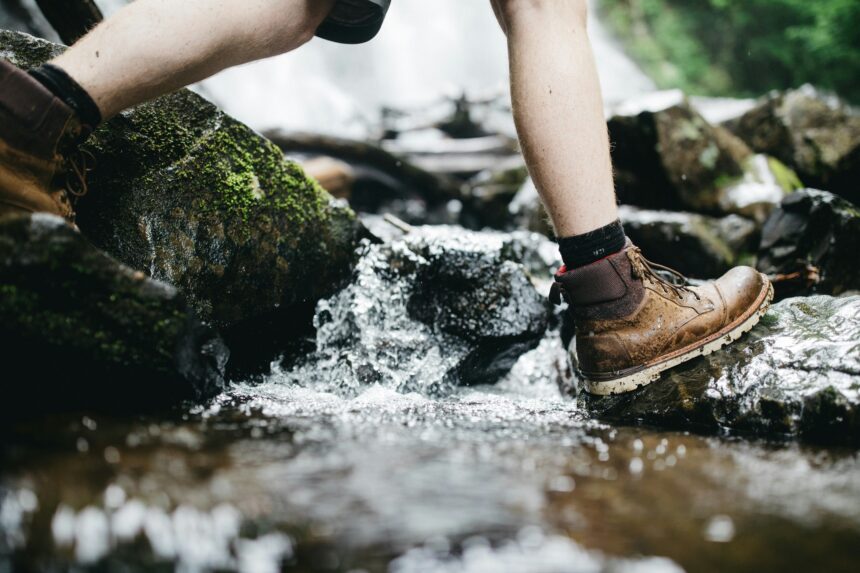 Hiker wearing muddy boots crossing rocks in a stream