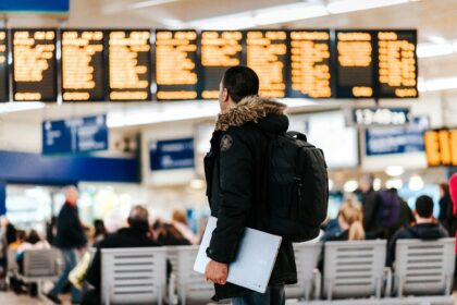Traveler wearing the best carry-on backpack for international travel while checking the airport departure board