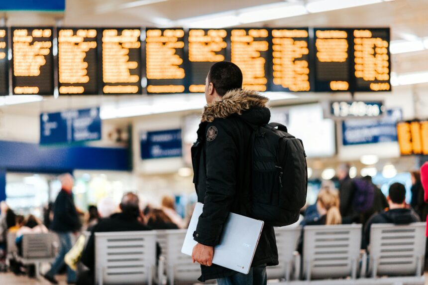 Traveler wearing the best carry-on backpack for international travel while checking the airport departure board