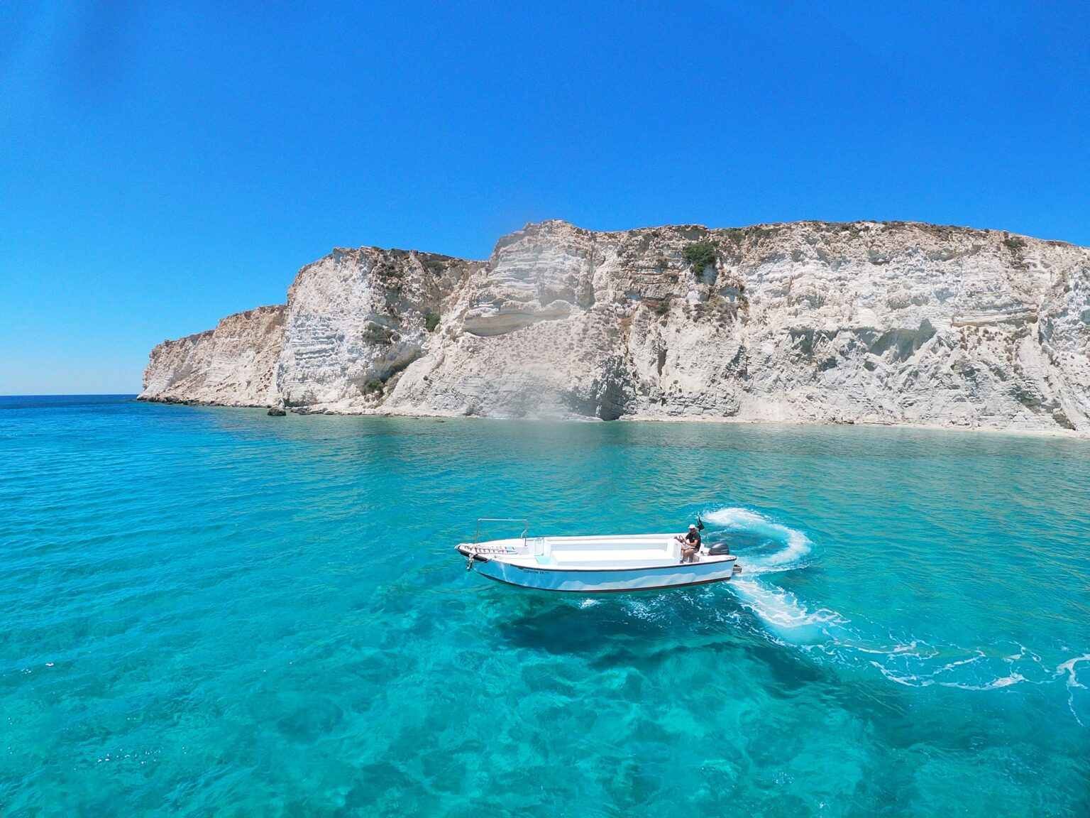 Turquoise sea and white cliffs with a boat, one of the best beaches in Greece.