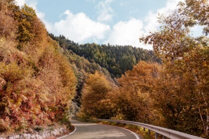Winding mountain road through gold and rust autumn forest, one of the best places to travel in October