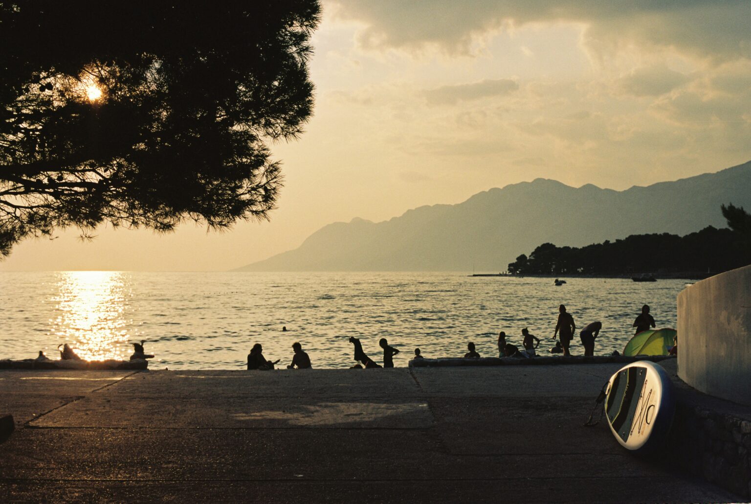 Sunset beach scene with people by the sea and mountains in the background for where to travel in summer.
