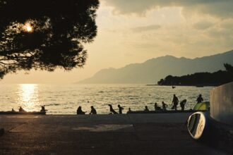 Sunset beach scene with people by the sea and mountains in the background for where to travel in summer.