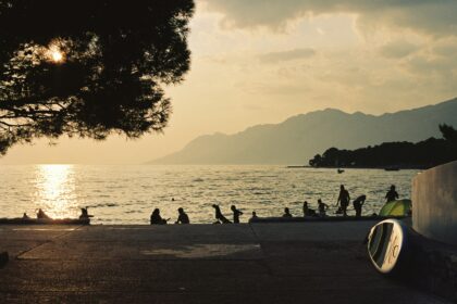 Sunset beach scene with people by the sea and mountains in the background for where to travel in summer.