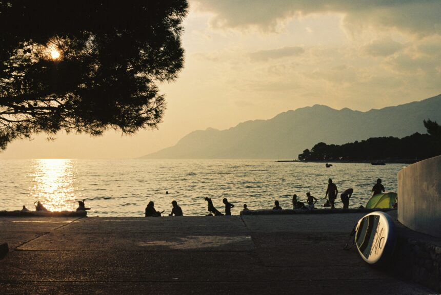 Sunset beach scene with people by the sea and mountains in the background for where to travel in summer.