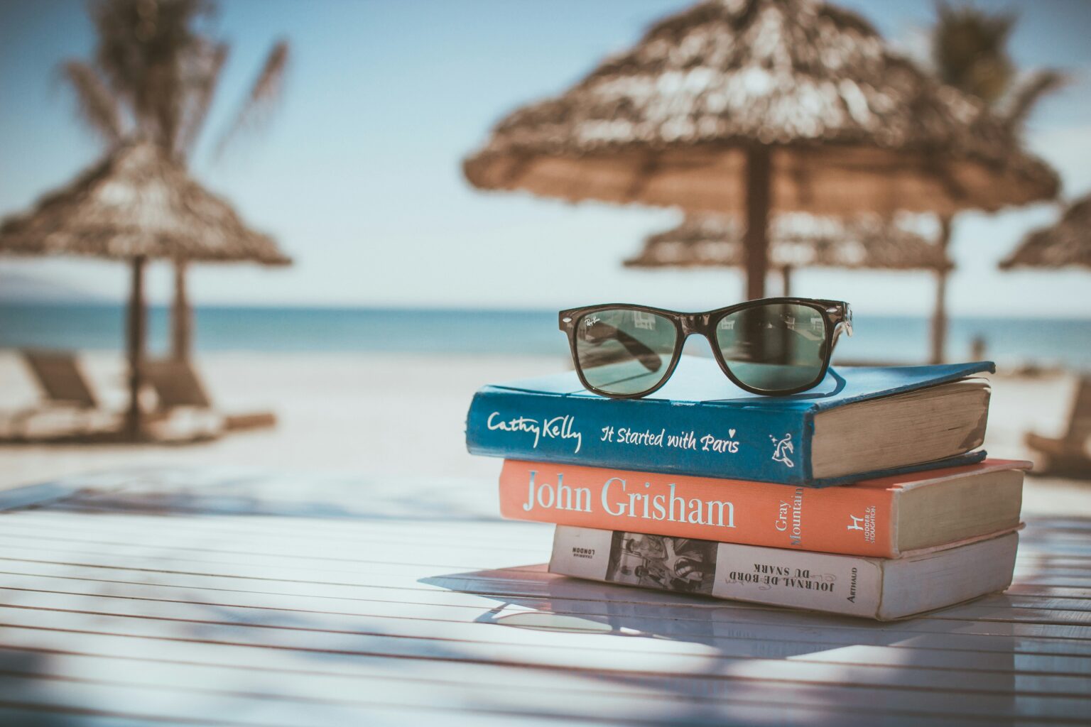 A stack of books and sunglasses on a beach table, the kind of scene readers picture when asking what is a travel blog