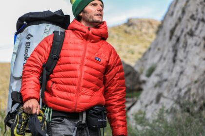Hiker in a red jacket carrying climbing gear in the mountains.