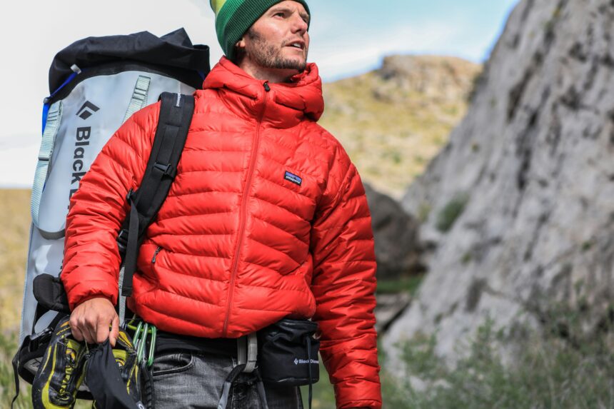 Hiker in a red jacket carrying climbing gear in the mountains.