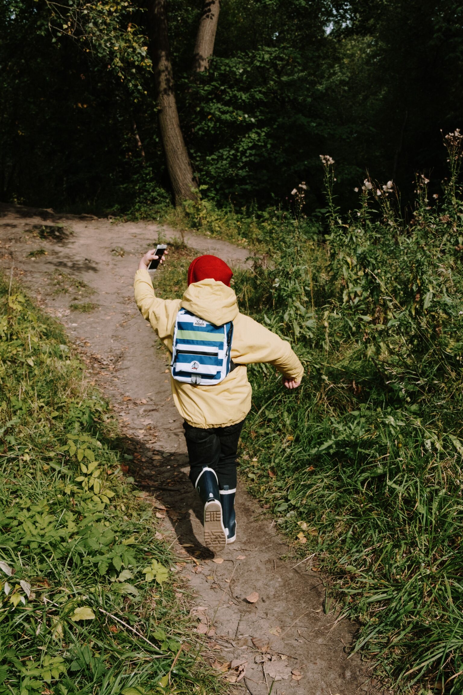 Toddler hiking boots shown on a small child walking on a soft woodland path